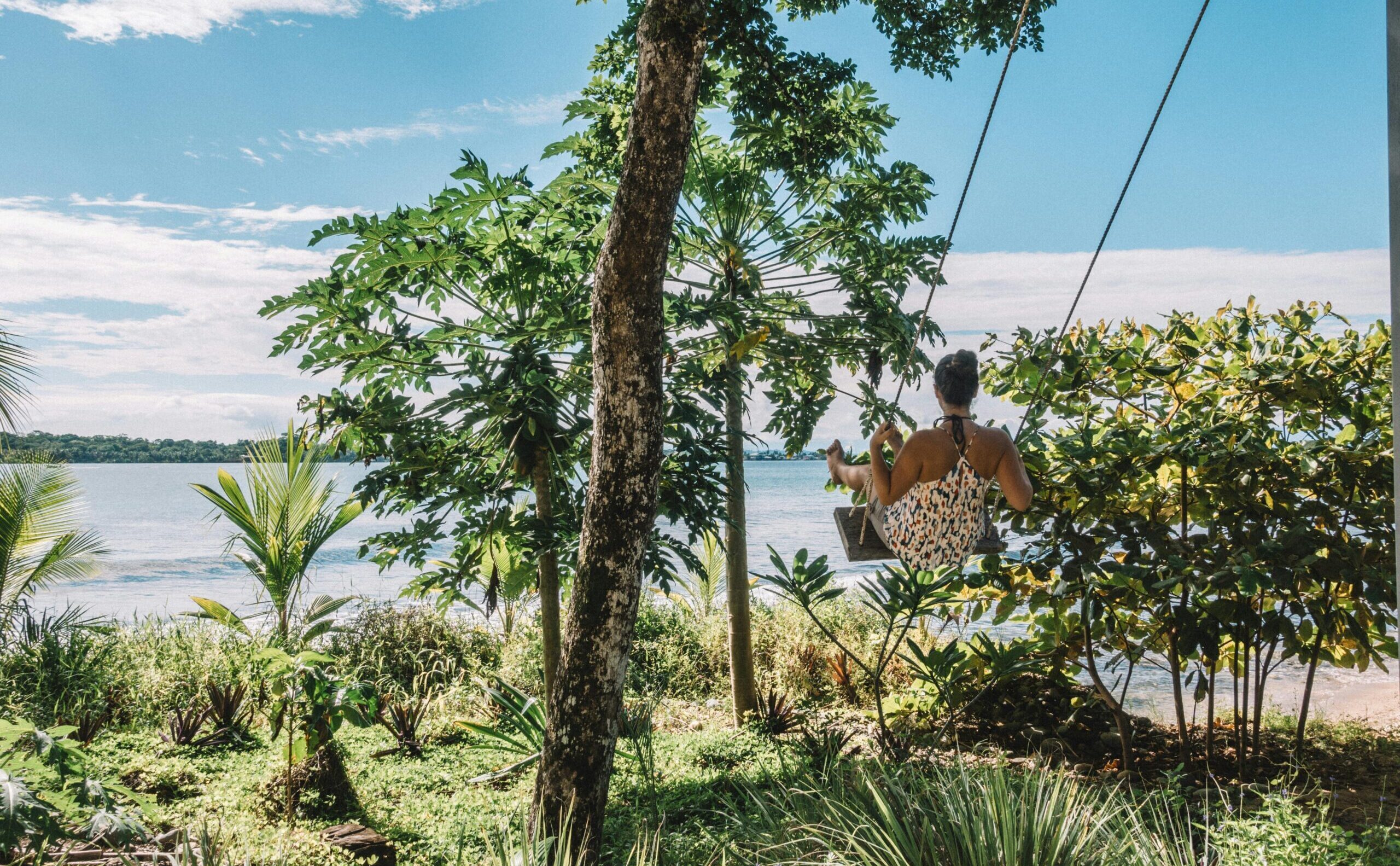 A woman enjoys a swing by the beach, surrounded by lush tropical greenery, capturing the essence of tranquility in Panama.