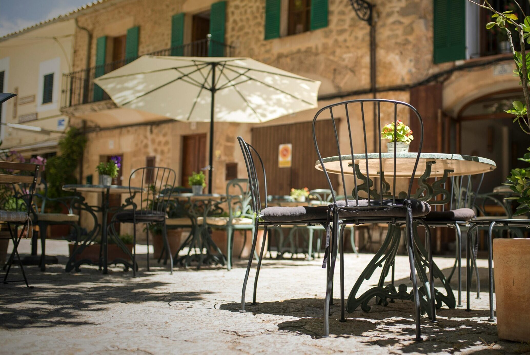 A quaint outdoor café in Mallorca, Spain, with iron chairs and rustic stone buildings.