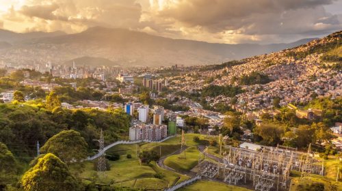 Aerial shot of Medellin, Colombia, showcasing urban sprawl and hills at sunset.