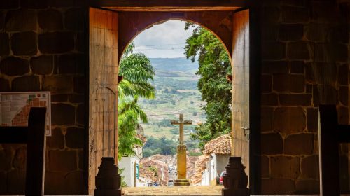 View through a church entrance in Barichara, Colombia, with a stone cross outdoors.