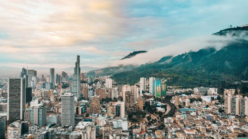 Dramatic aerial shot of Bogotá's skyline with mountain backdrop and clouds.